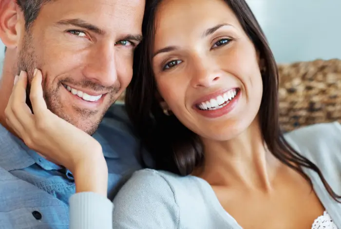Smiling woman next to a smiling man holding his face