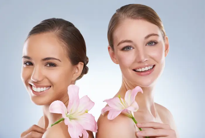 Two smiling women each holding a pink flower