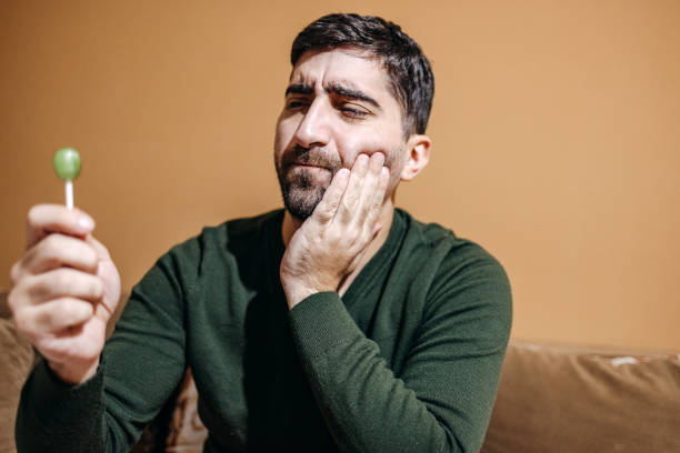 a man pressing his jaw due to tooth pain while holding up a lollipop in front of him